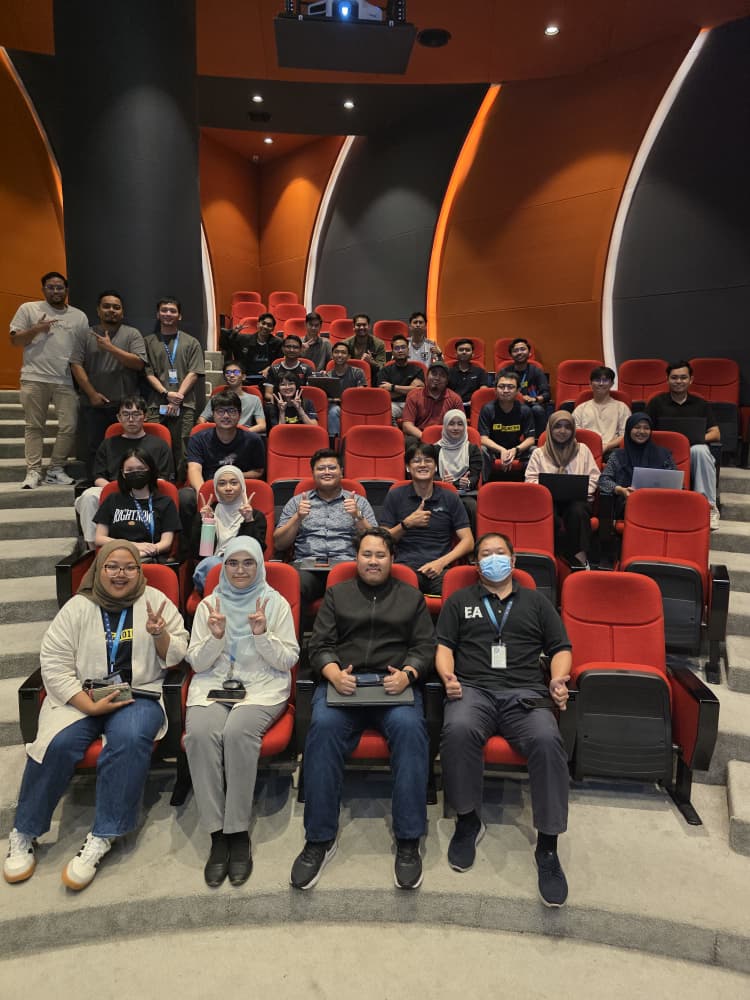 Colleagues seated in the auditorium and smiling for a group photo after the Tech Harbour session